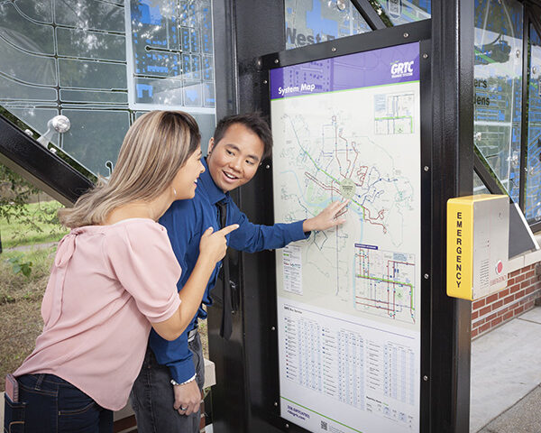 A man and woman looking at a bus schedule at a bus station