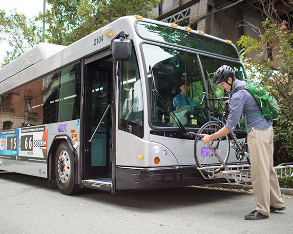 A man uses the bus bike rack at the front of the bus before getting on the bus.