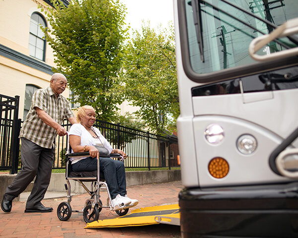 An older gentleman pushes his wife in a wheelchair, onto the bus ramp.