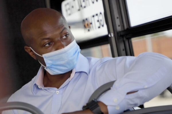 Masked man in suit riding bus