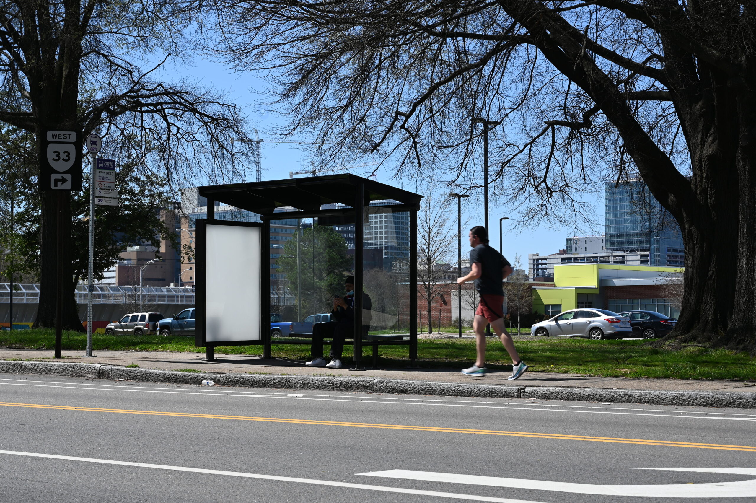 New shelter at bus stop 1833 Mosby & P showing passenger seated and runner approaching with City skyline in background