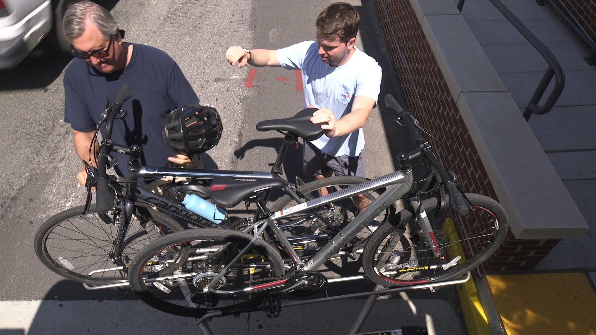 Two adult men loading their bikes onto the bike racks at the front of the bus