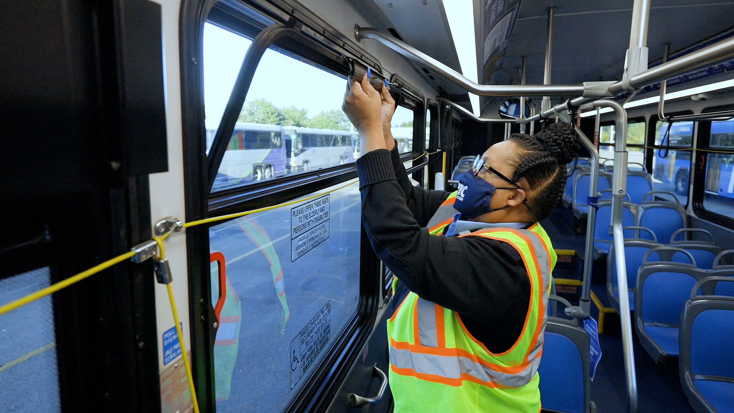 Bus Operator wearing mask and safety vest with uniform opens a window on the bus before service.