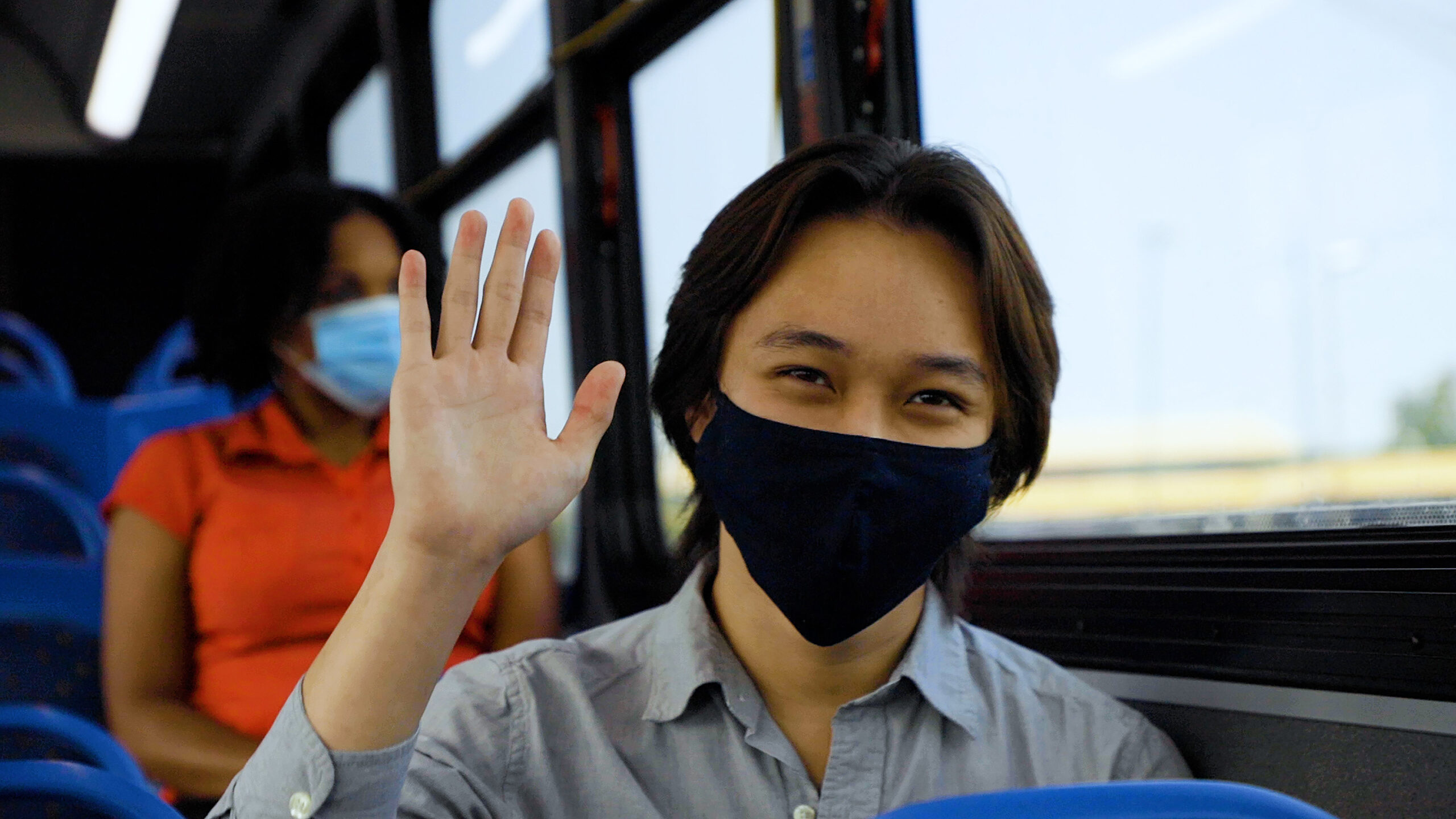 Male bus rider in a mask waving at you